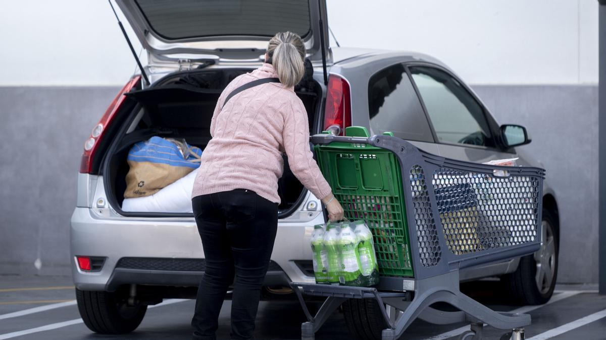 Una mujer mete la compra en el maletero de su vehículo al salir de un supermercado.