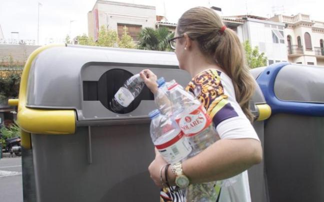 Una mujer deposita varias botellas de plástico en un contenedor de la calle Muro.