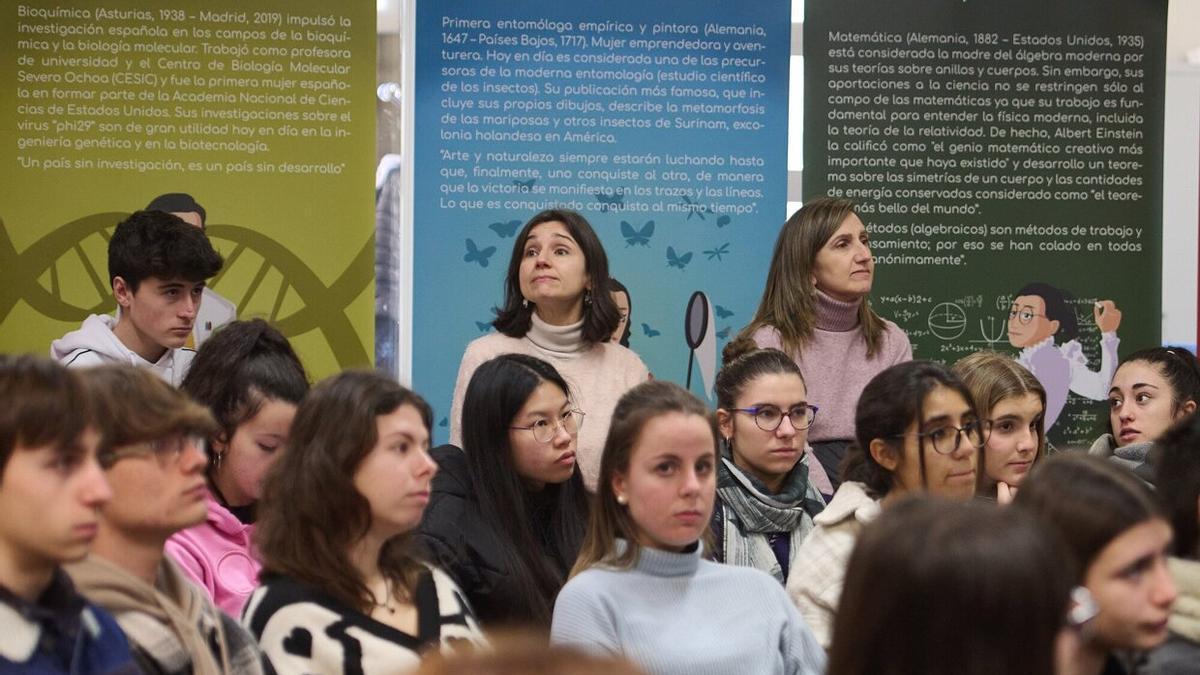 Alumnos escuchan las intervenciones en la biblioteca de la UPNA, con la exposición 'Científicas en la Historia' detrás.