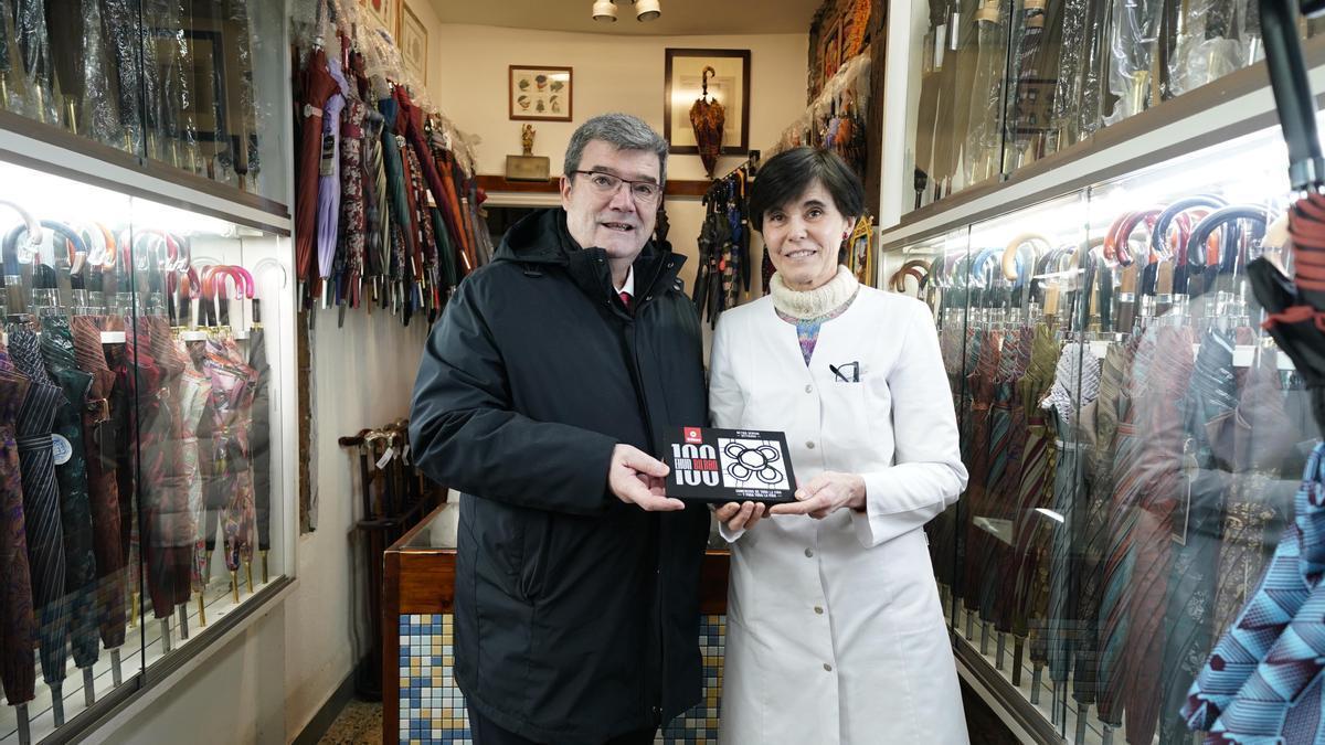 Juan Mari Aburto, alcalde de Bilbao, posa con Lourdes Leoz sosteniendo la baldosa que acredita que su paragüería es un 'comercio centenario'