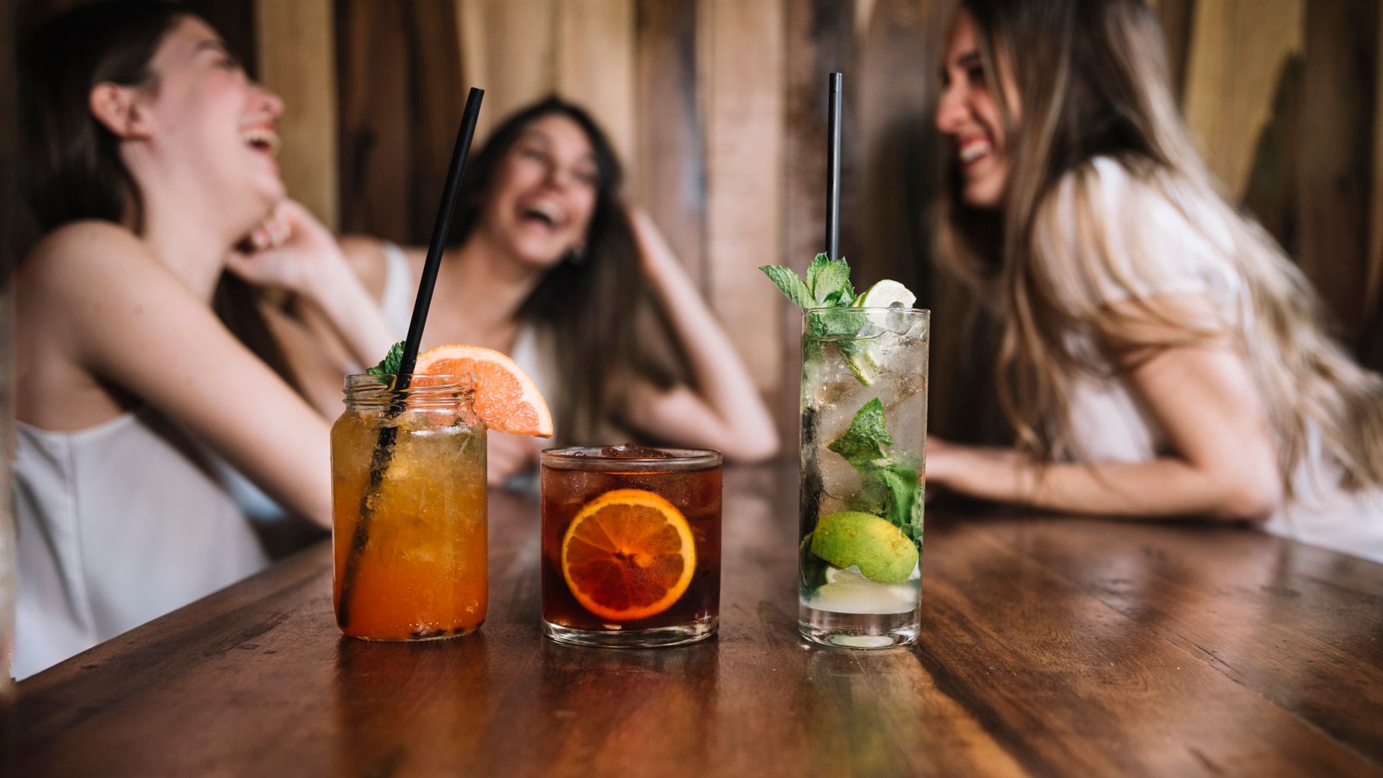 Tres amigas ríen mientras toman unos combinados.