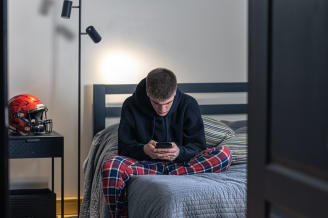 Un adolescente mira la pantalla del móvil en su habitación.