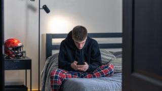 Un adolescente mira la pantalla del móvil en su habitación. Un adolescente mira la pantalla del móvil en su habitación.
