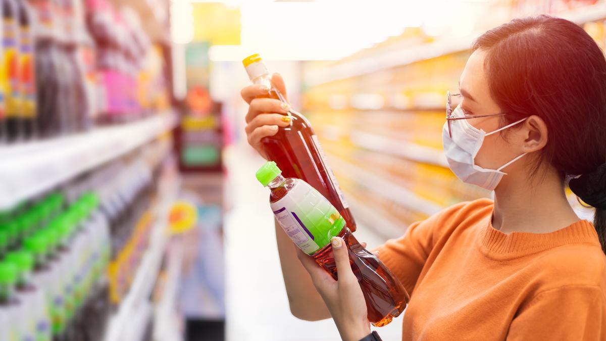 Una clienta de un supermercado examina las etiquetas de dos botellas.