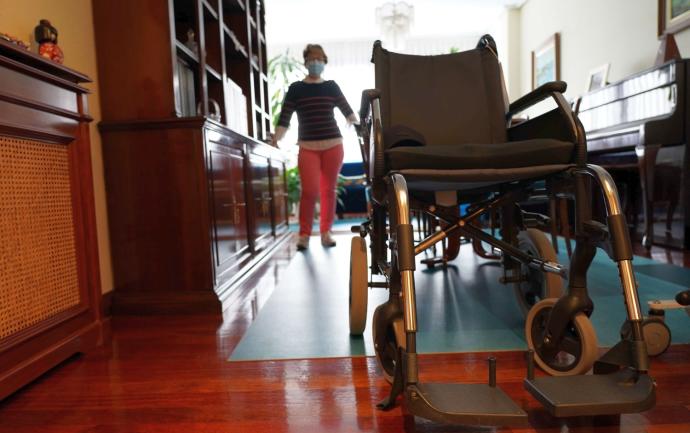Garbiñe, en el salón de su domicilio, en Galdakao, con la silla de ruedas de Humberto, que camina con mucha dificultad, en primer plano.