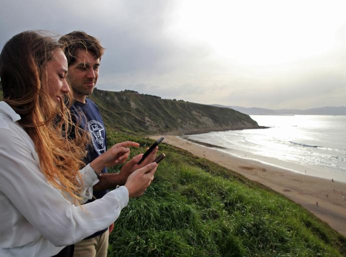 Tatiana y Luis Martínez de las Rivas Álvarez consultan desde sus teléfonos móviles su plataforma 'Foamsurfing' frente a la playa de Barinatxe de Sopela.