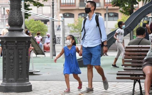 Una familia de origen asiático camina por El Arenal mientras al fondo, sentadas en un banco, un par de mujeres africanas pasan la tarde charlando.