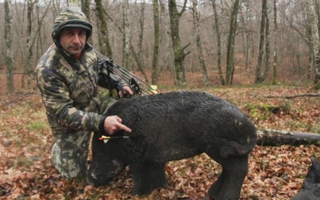 Un arquero posa junto a una figura de un jabalí.