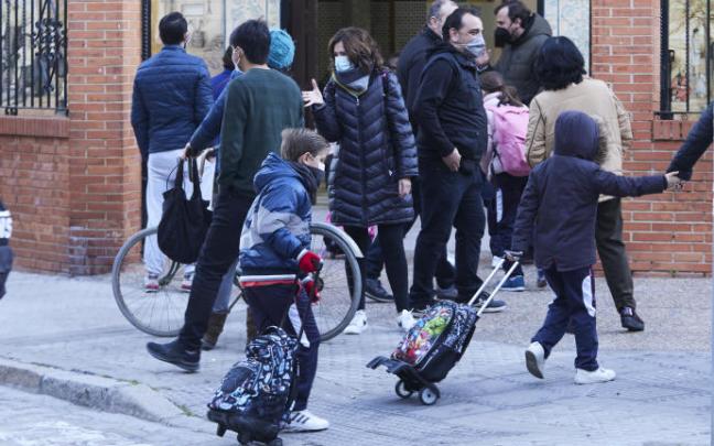 Unos niños cruzan un paso de peatones a la entrada de un colegio.