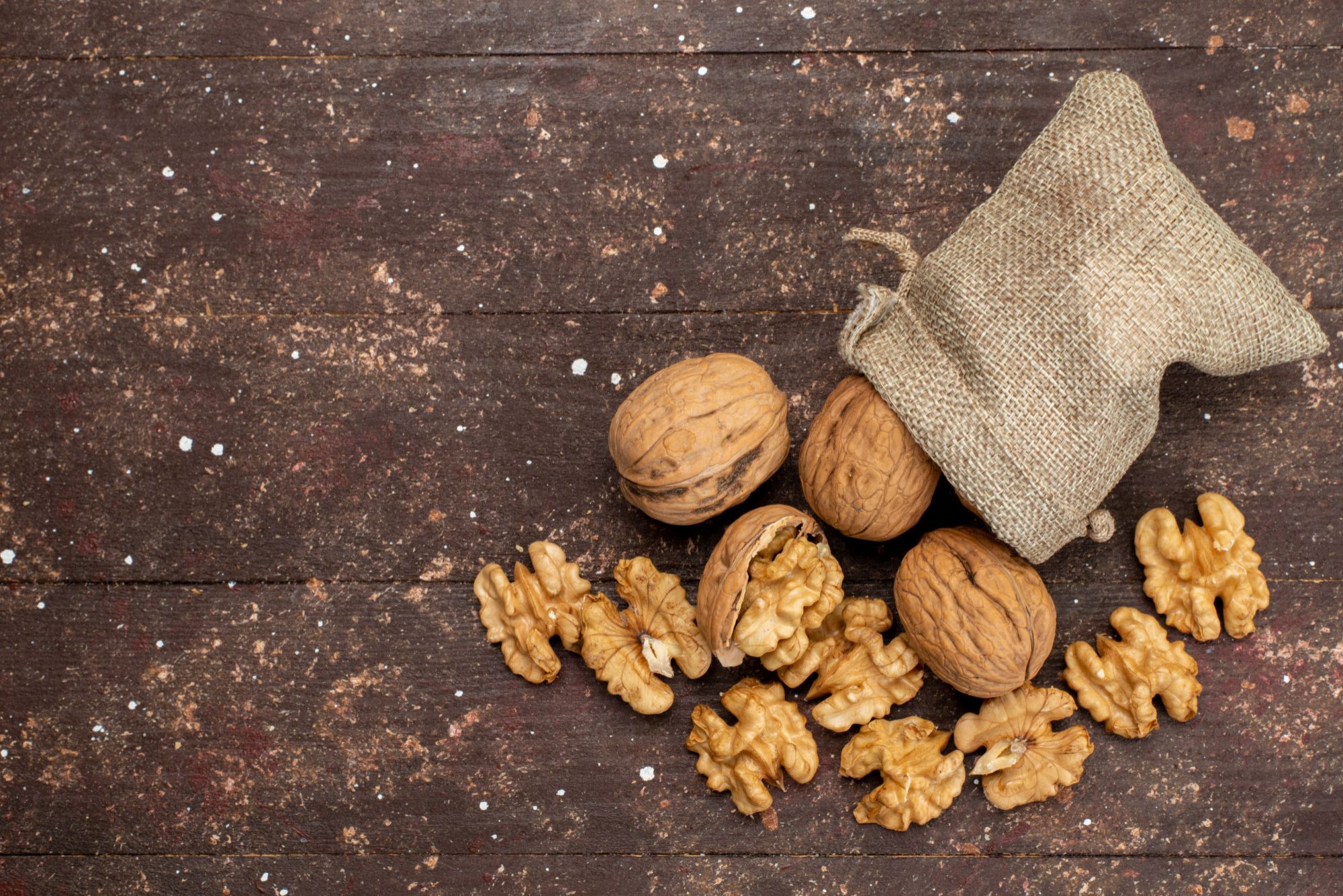 Un pequeño saco junto a nueces desparramadas por la mesa.