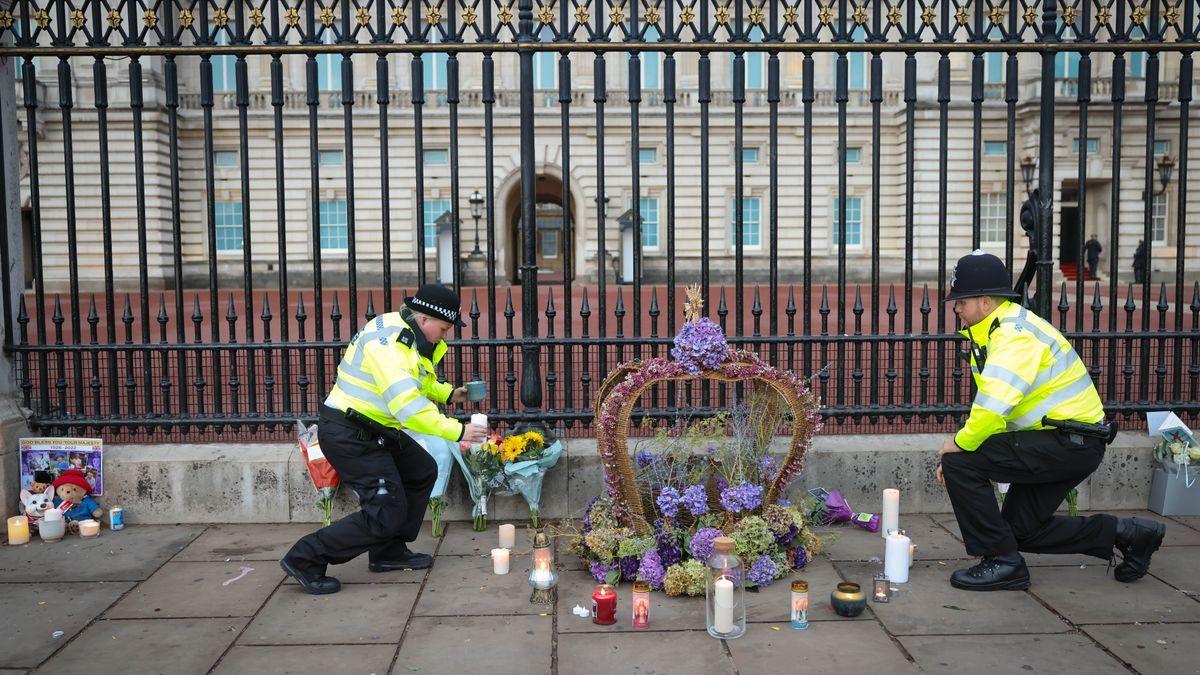 Dos agentes de policía depositan velas y flores a las puertas del Palacio de Buckingham.