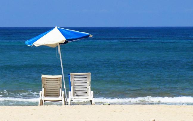 Una sombrilla junto a dos tumbona en una playa de arena blanca.