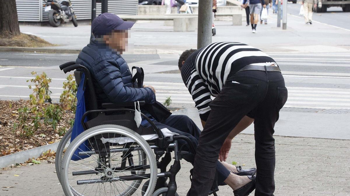 Una persona mayor en silla de ruedas con su cuidador.