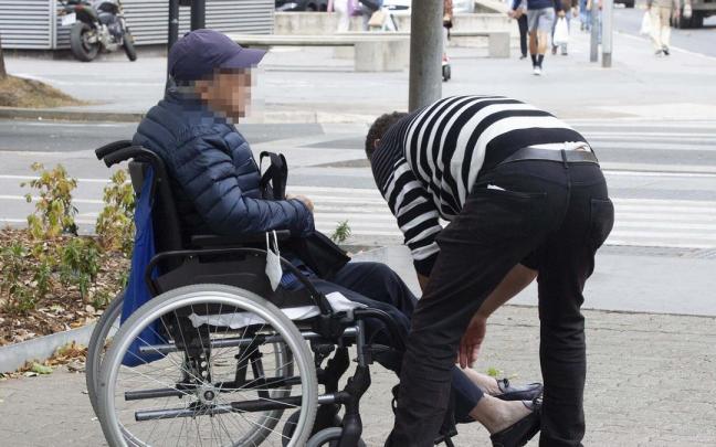 Una persona mayor en silla de ruedas con su cuidador.