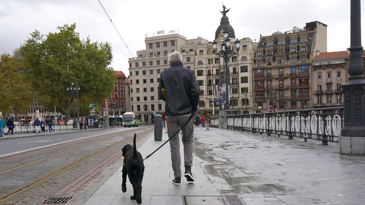 Un hombre pasea con su perro por el puente de El Arenal de Bilbao.