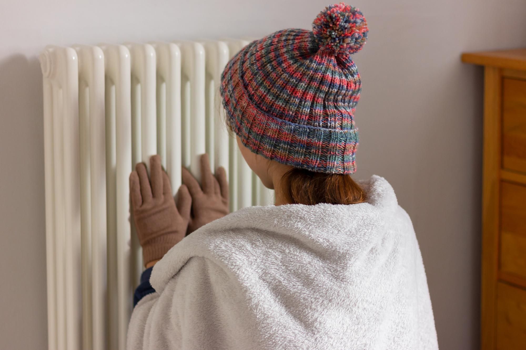 Una mujer pone sus manos con guantes en un radiador.
