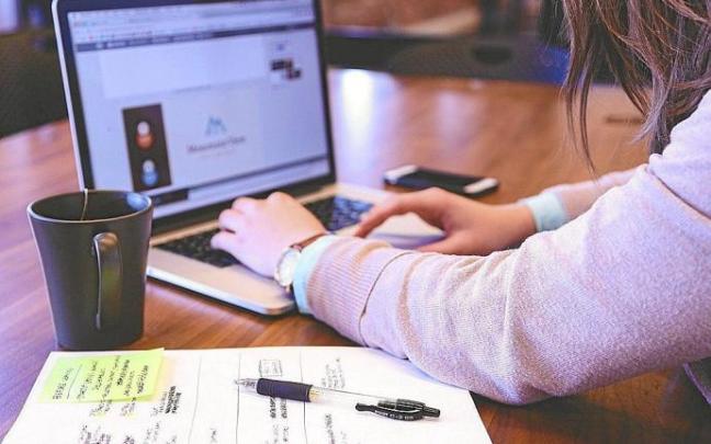 Una mujer, en su puesto de trabajo, maneja un ordenador portátil junto a una hoja con apuntes. Foto: Pixabay