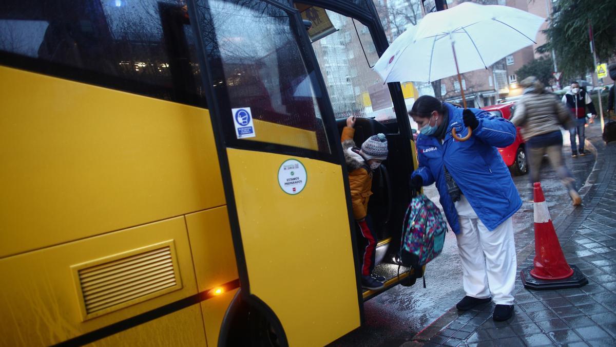 Una trabajadora ayuda a bajar a un alumno de un autobús escolar.