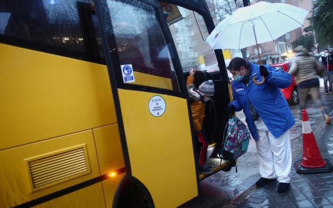 Una trabajadora ayuda a bajar a un alumno de un autob&uacute;s escolar.