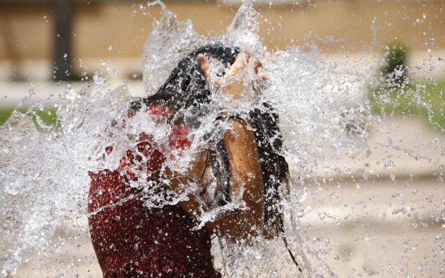 Una niña se refresca en una fuente durante una ola de calor Una niña se refresca en una fuente durante una ola de calor