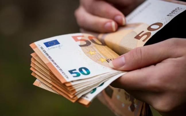 Una persona cuenta su dinero en efectivo en fajos de billetes de cincuenta.