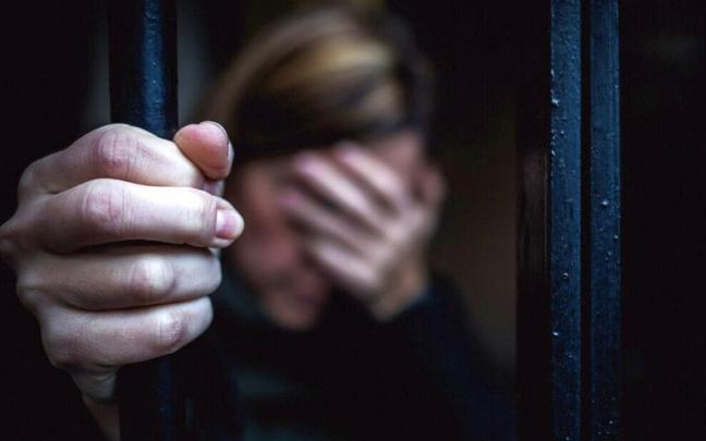 Una mujer se tapa la cara agarrada a una verja.