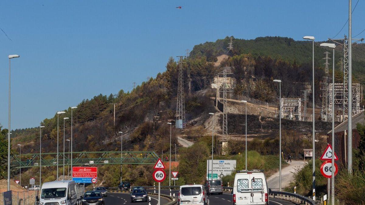 Vehículos circulando por la Ronda de Pamplona, con el monte quemado al fondo.