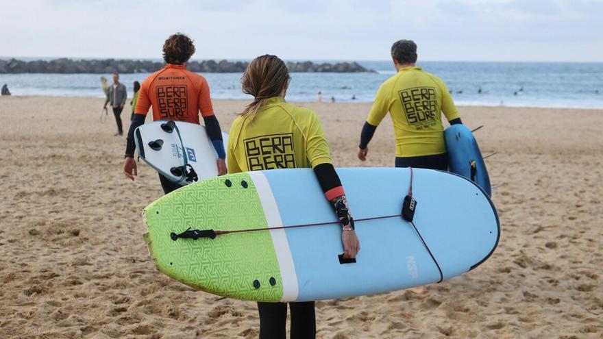 Dos alumnos y el monitor se dirigen al agua para surfear.