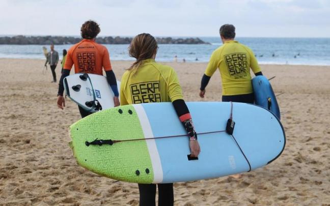 Dos alumnos y el monitor se dirigen al agua para surfear. Dos alumnos y el monitor se dirigen al agua para surfear.