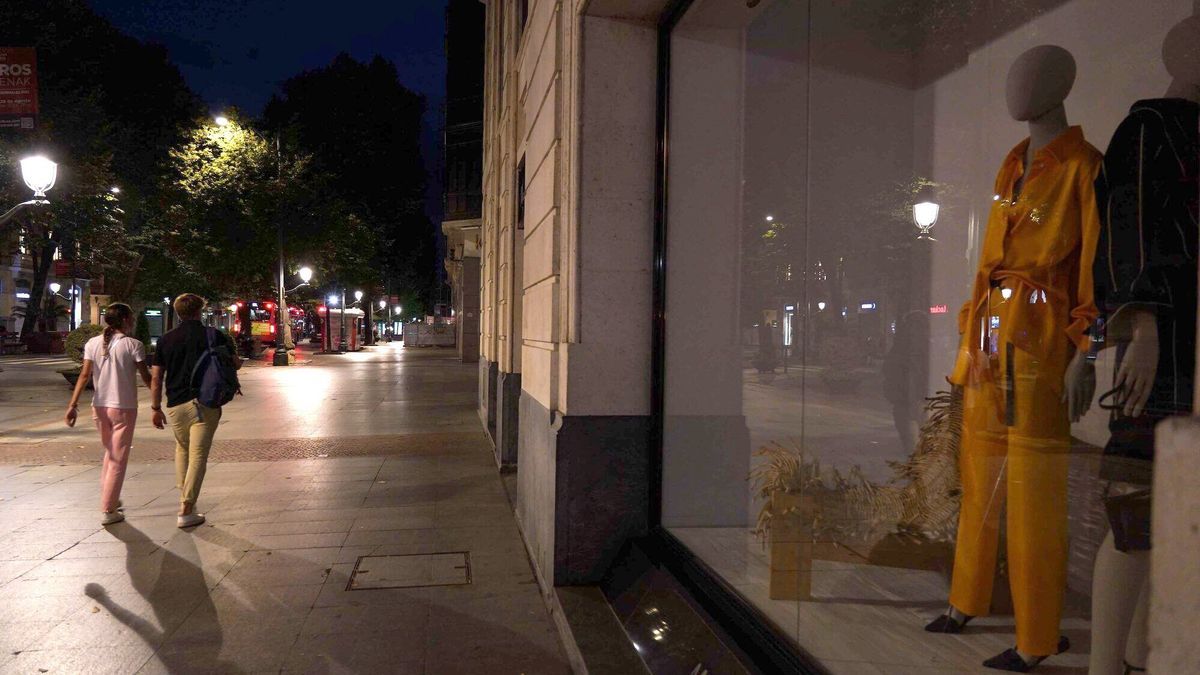 Varias personas caminan por la Gran Vía de Bilbao con las luces de los comercios apagadas