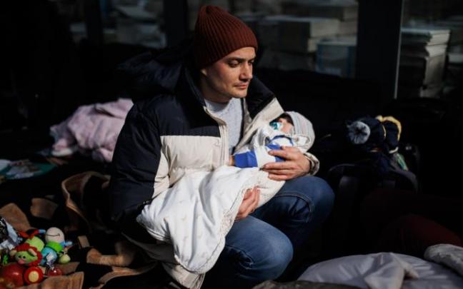 Una hombre sostiene un bebé, en un centro comercial habilitado para los refugiados, en Mylny, (Polonia).