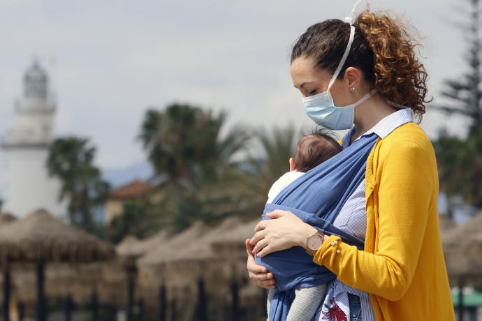 Una mujer pasea con su bebé con una mascarilla.