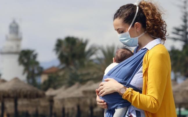 Una mujer pasea con su bebé con una mascarilla.