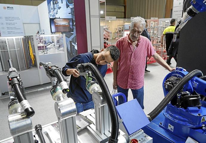 Unos visitantes observan los productos de un expositor de la Bienal de Máquina Herramienta.