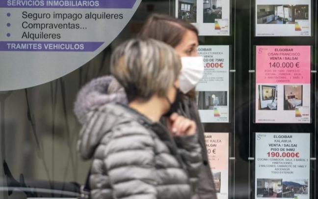 Dos personas caminan por delante del escaparate de una inmobiliaria. Dos personas caminan por delante del escaparate de una inmobiliaria.