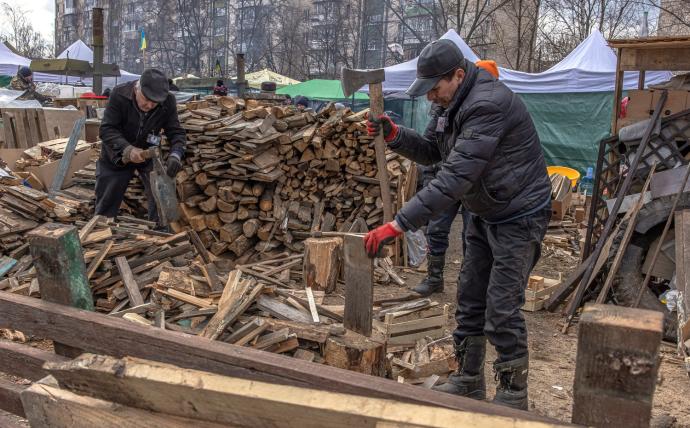 Dos hombres ucranianos cortan madera en Kiev en uno de los campamentos improvisados.