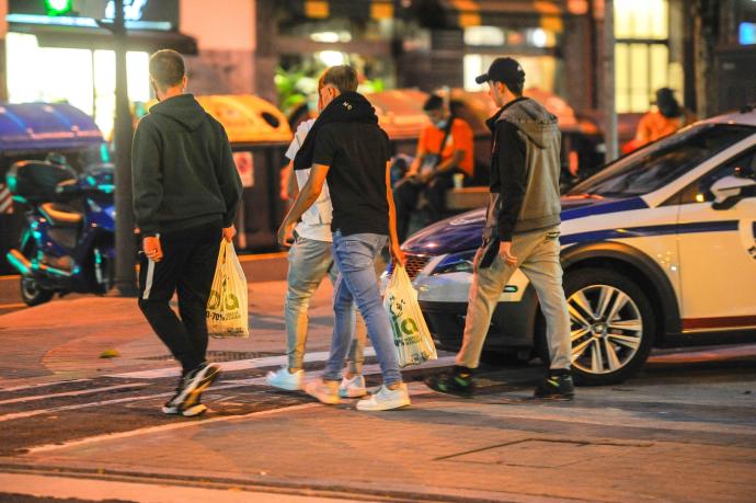 Jóvenes pasan con bolsas junto a un coche de la Ertzaintza, ayer, en la calle Licenciado Poza de Bilbao, donde se vienen produciendo incidentes por el botellón.