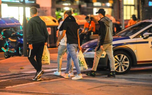 Jóvenes pasan con bolsas junto a un coche de la Ertzaintza, ayer, en la calle Licenciado Poza de Bilbao, donde se vienen produciendo incidentes por el botellón. Jóvenes pasan con bolsas junto a un coche de la Ertzaintza, ayer, en la calle Licenciado Poza de Bilbao, donde se vienen produciendo incidentes por el botellón.