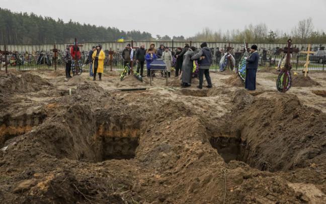 Varias personsa asisten a un entierro en el cementerio de Bucha.