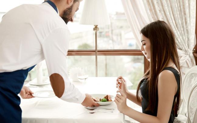 Un camarero sirve una comida a una clienta.