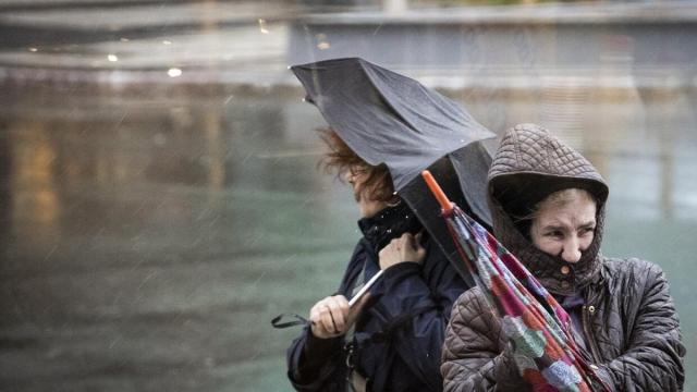 Dos mujeres tratan de protegerse este martes en Donostia de las fuertes rachas de viento y de las intensas lluvias que ha tra&iacute;do el temporal 'Gerard'.