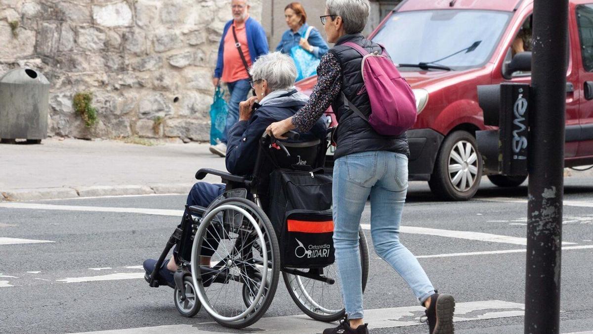 Una persona mayor en silla de ruedas con su cuidadora.