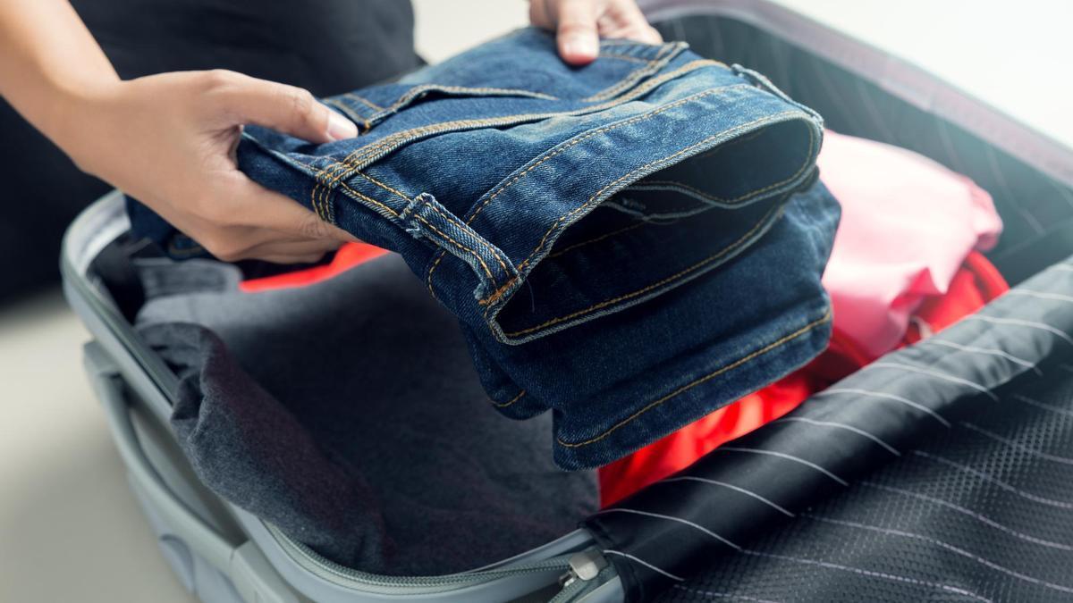 Una persona mete un pantalón en una maleta de cabina o de mano.