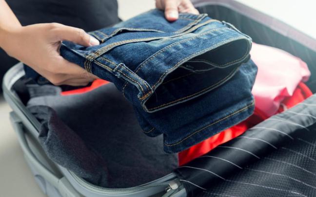 Una persona mete un pantal&oacute;n en una maleta de cabina o de mano.