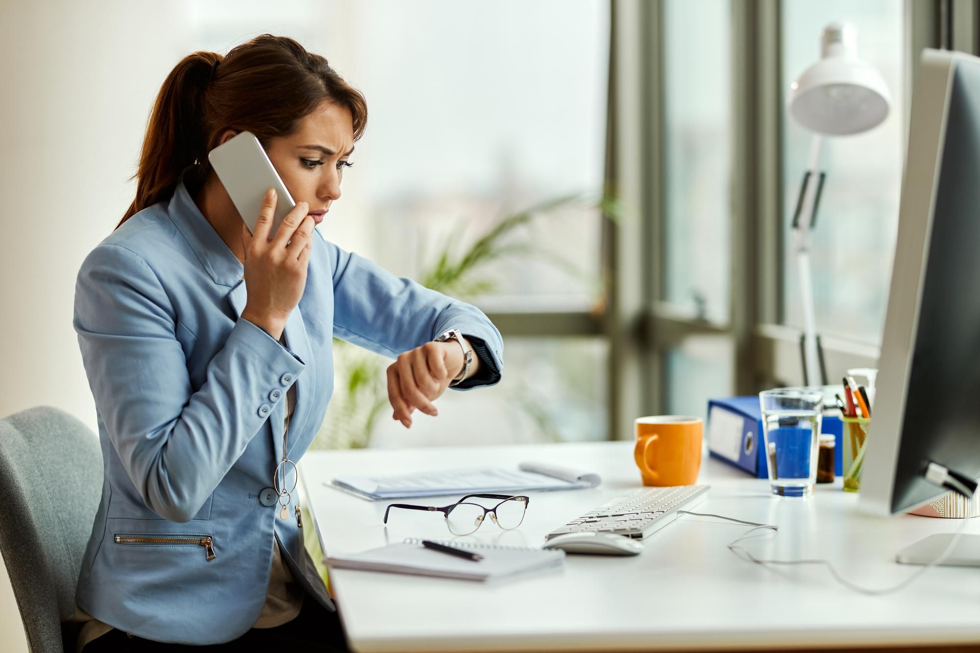 Una mujer mira el reloj mientras habla por teléfono en su trabajo.