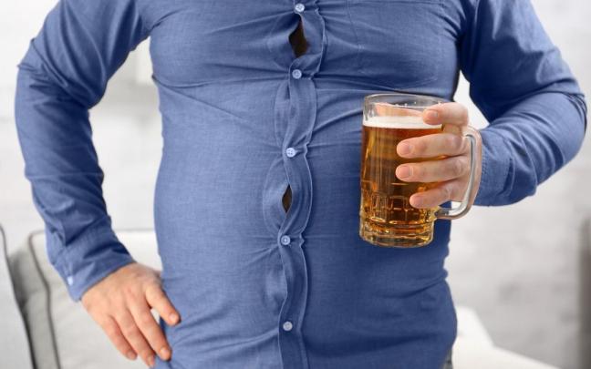 Un hombre con la camisa demasiado apretada sostiene una cerveza. Un hombre con la camisa demasiado apretada sostiene una cerveza.