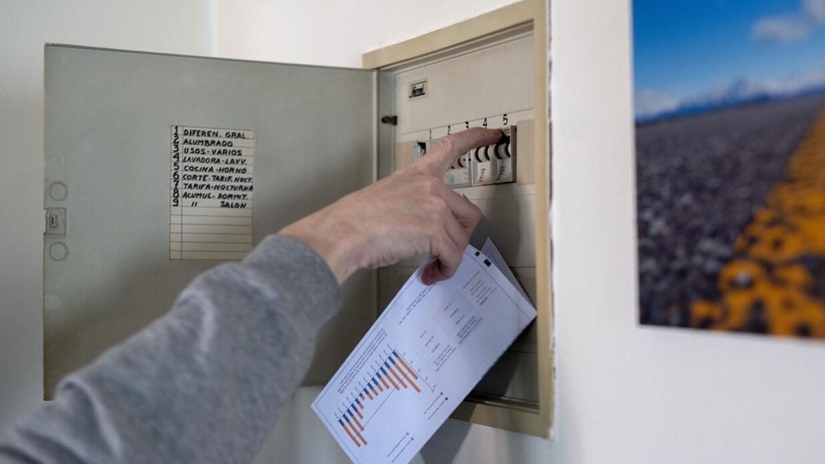 Un hombre con una factura de la luz en la mano manipula una cuadro eléctrico