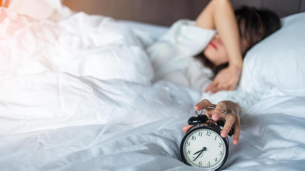 Una mujer en la cama a punto de apagar el despertador.