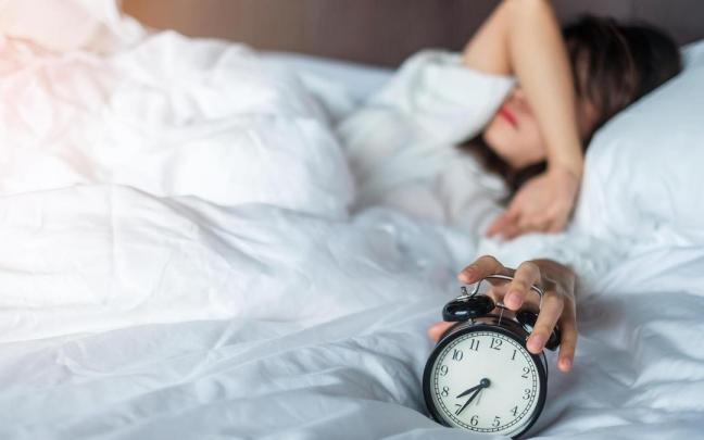 Una mujer en la cama a punto de apagar el despertador.