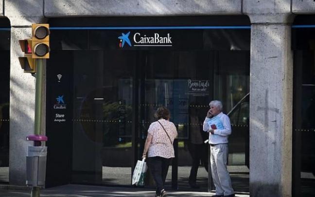 Dos personas pasan frente a una oficina de Caixabank.